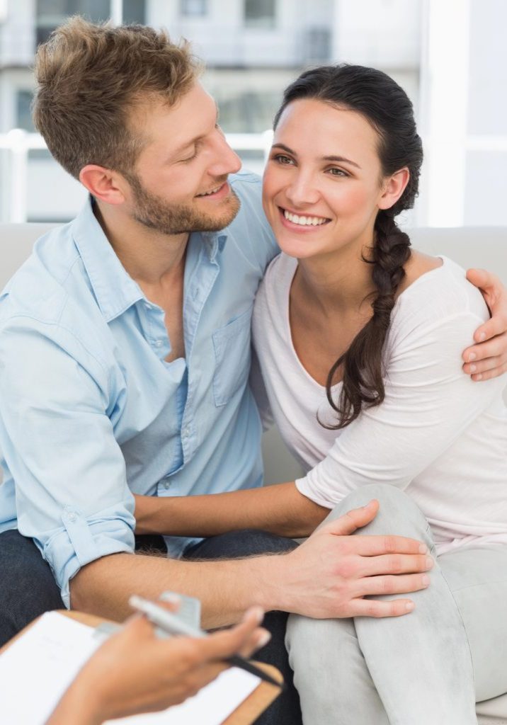 A couple smiling while sitting with a counselor